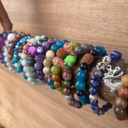 colorful beaded children's bracelets on a wooden rod, featuring a variety of gemstone beads, charms like a silver dragon and a green elephant