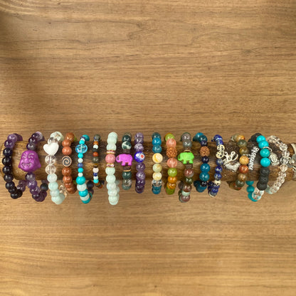 colorful beaded children's bracelets on a wooden rod, featuring a variety of gemstone beads, charms like a Buddha face, and small animal figures.