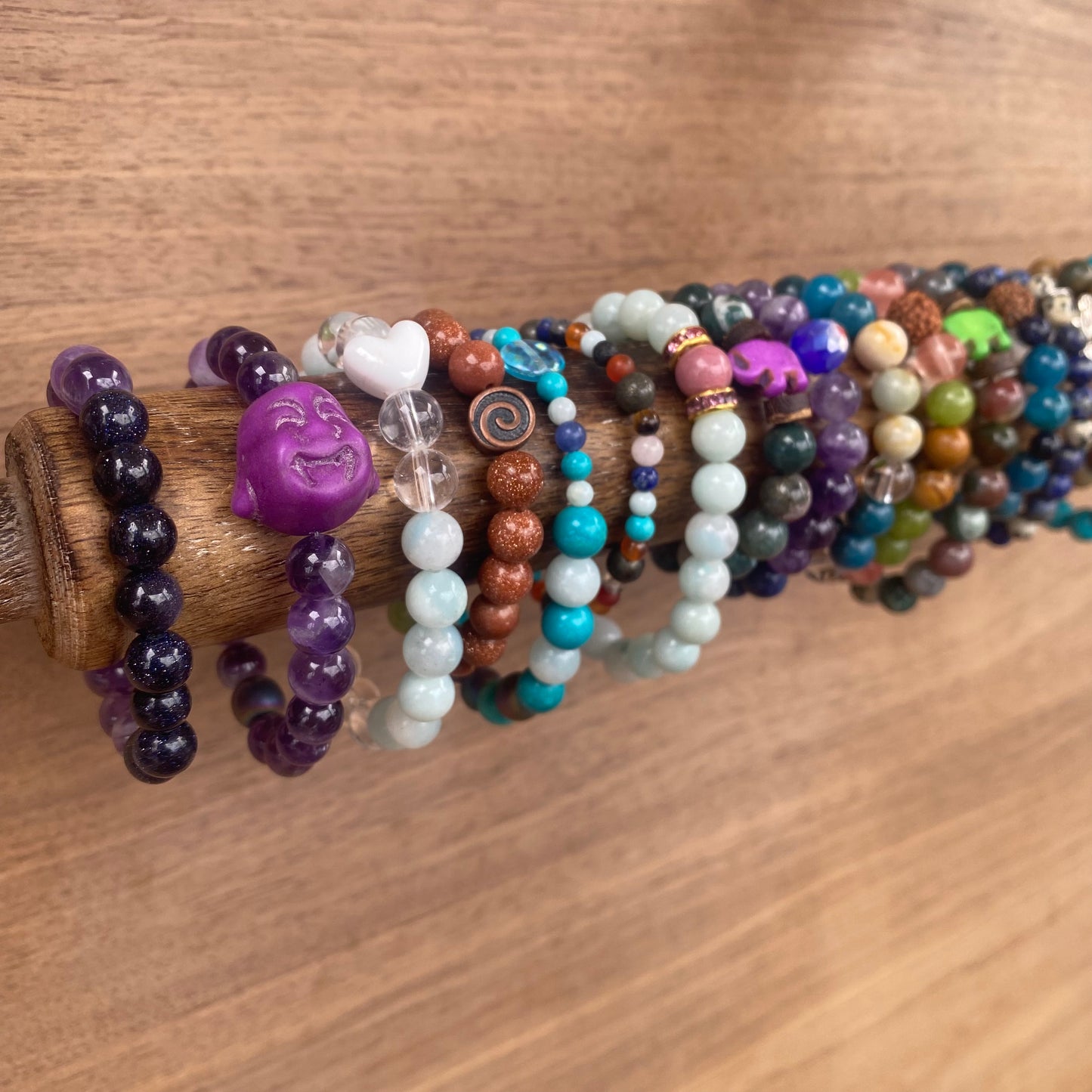 colorful beaded children's bracelets on a wooden rod, featuring a variety of gemstone beads, charms like a Buddha face, elephant and a heart.